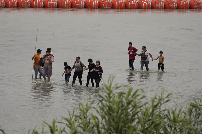 Migrants who crossed the Rio Grande from Mexico walk past large buoys being deployed as a border barrier on the river in Eagle Pass, Texas, on Wednesday.