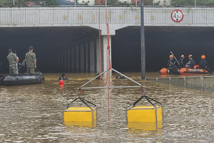 In this photo provided by South Korea National Fire Agency, rescuers search along a road submerged by floodwaters leading to an underground tunnel in Cheongju, South Korea,  on Sunday.