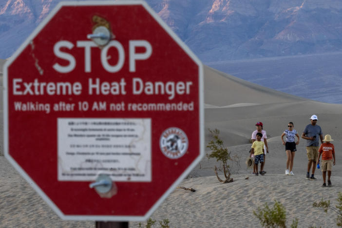 People walk among sand dunes near a sign warning of extreme heat danger in Death Valley National Park on Saturday.