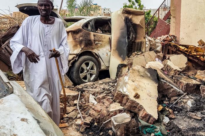 A man inspects damage as he walks through the rubble by a destroyed car outside a house that was hit by an artillery shell in the Azhari district in the south of Khartoum on June 6, 2023.