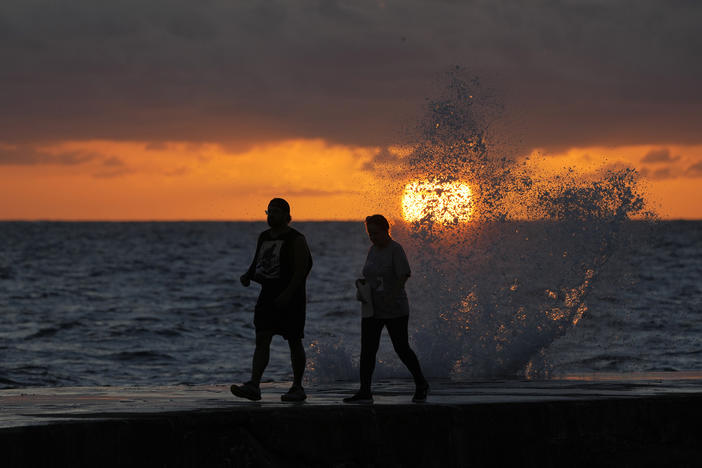 The sun rises above the Atlantic Ocean as waves crash near beachgoers walking along a jetty. Ocean temperatures averaged five degrees warmer around South Florida beginning in July.