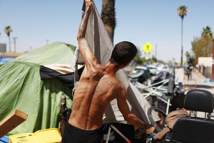 A homeless person adjusts a friend's tent to help increase shade cover in a section of The Zone, Phoenix's largest homeless encampment.