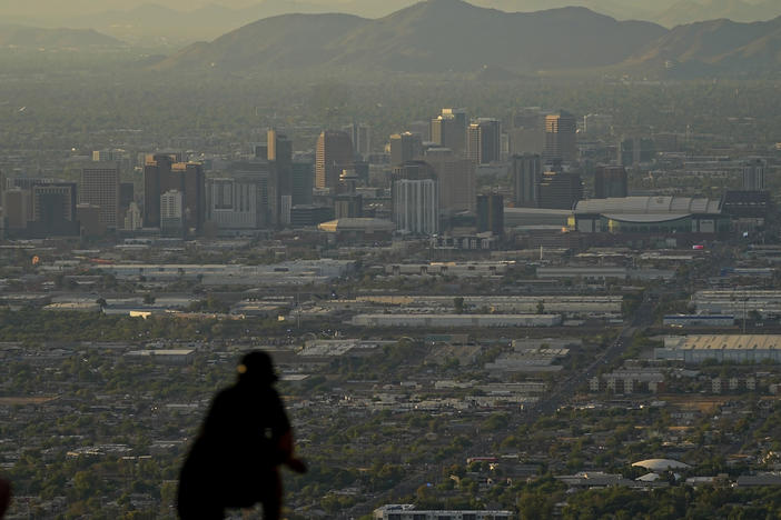 A man overlooks downtown Phoenix at sunset atop South Mountain, Sunday, July 30, 2023. Some slight relief may be on the way as seasonal thunderstorms could drop temperatures in Phoenix on Monday and Tuesday. (AP Photo/Matt York)