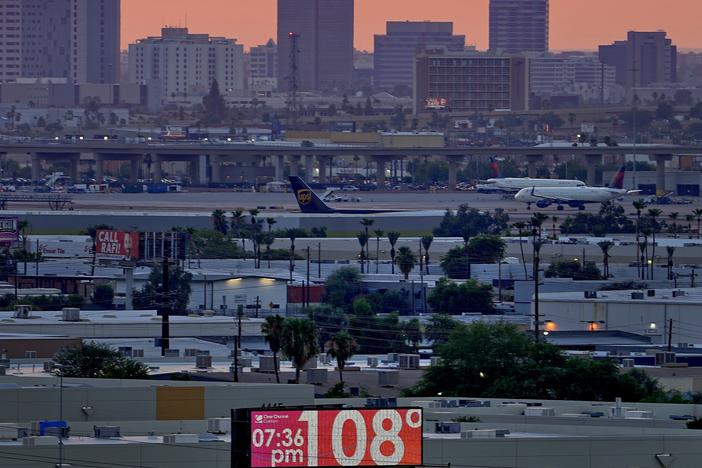 A sign displays an an unofficial temperature as jets taxi at Sky Harbor International Airport at dusk, July 12 in Phoenix.