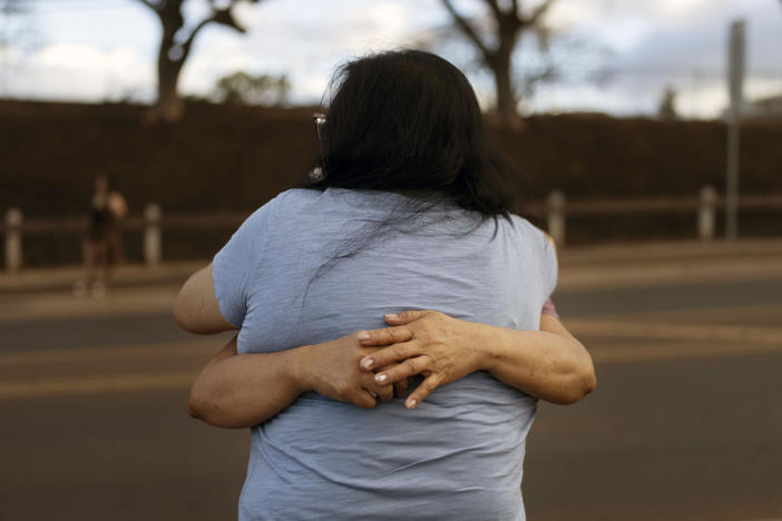 Carelle Calvan in blue T-shirt, hugs Nora Bulosan as they gather near a checkpoint in hopes to get access to their home destroyed in recent wildfires in Lahaina, Hawaii, Wednesday, Aug. 16, 2023.