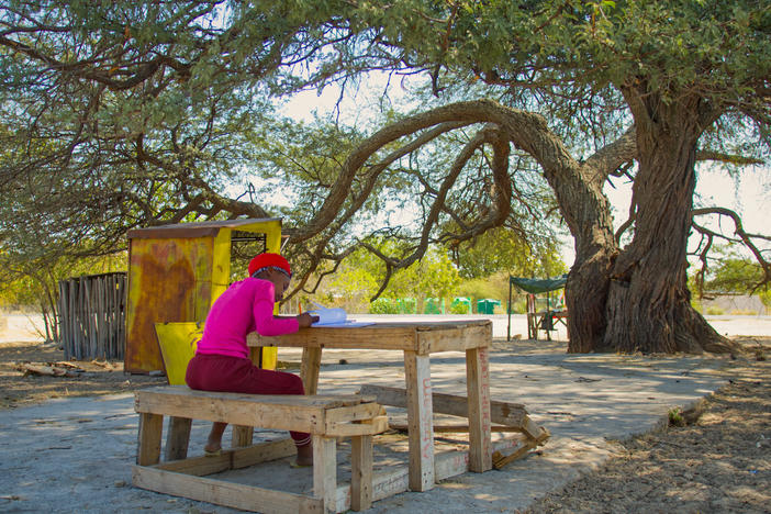 Teenage girl writes her school work under the tree while watching over the tuck shop.