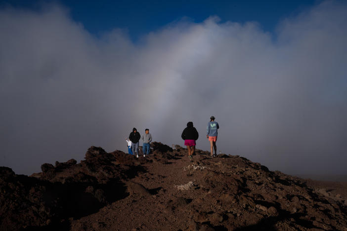 A few tourists stand under a rainbow as the clouds clear at Haleakalā on the island of Maui, Hawaii. Though much of the island is untouched, tourism is down drastically.