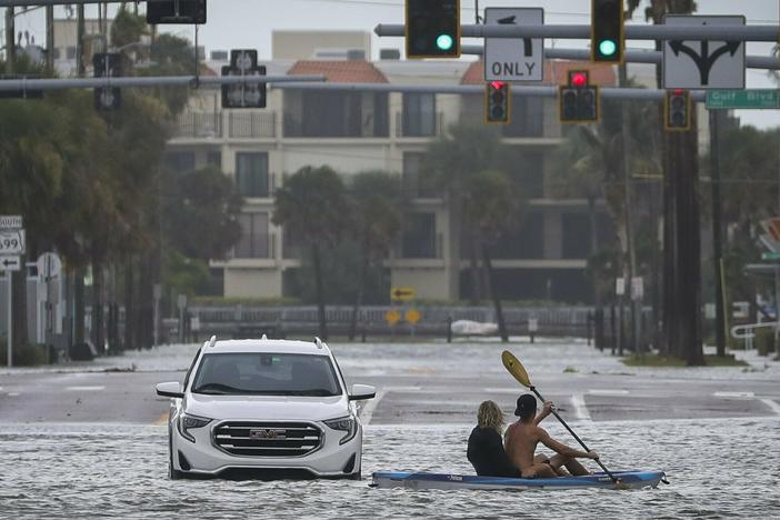 People kayak past an abandon vehicle in the intersection of Boca Ciega Drive and Pasadena Avenue Wednesday, Aug. 30, 2023 in St. Pete Beach, Fla.