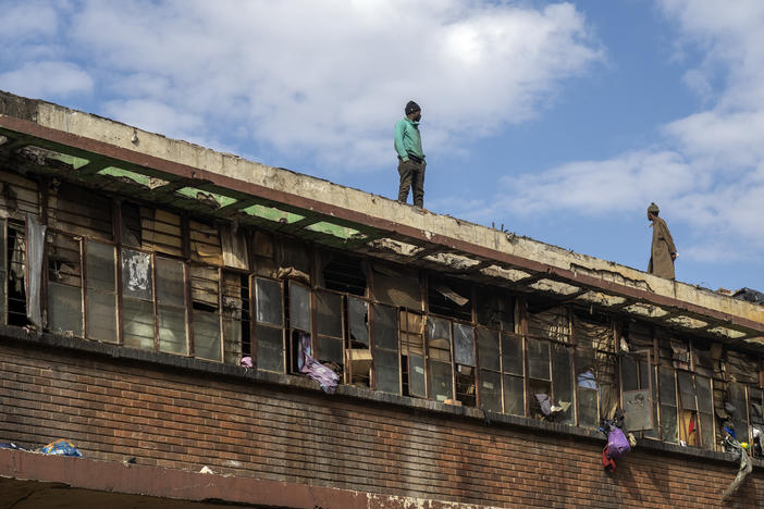 Squatters stand on a rooftop overlooking the scene of one of South Africa's deadliest inner-city fires in Johannesburg, South Africa, Friday.