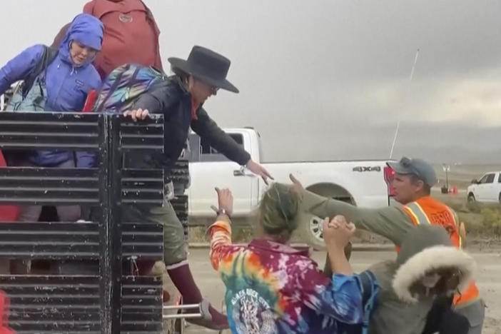 In this image from video provided by Rebecca Barger, festival-goers are helped off a truck from the Burning Man festival site in Black Rock, Nev., on Monday, Sept. 4, 2023.