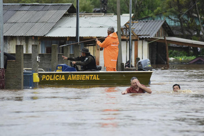 Police officers check a house as residents wade through a flooded street after floods caused by a cyclone in Passo Fundo, Rio Grande do Sul state, Brazil, Monday.