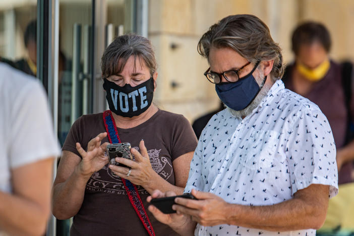 Voters check their phones while waiting to cast in-person ballots at a polling location in Austin, Texas, on Oct. 13, 2020. Many Americans wonder why they can't vote online, on their phones, but experts agree that it's not secure.