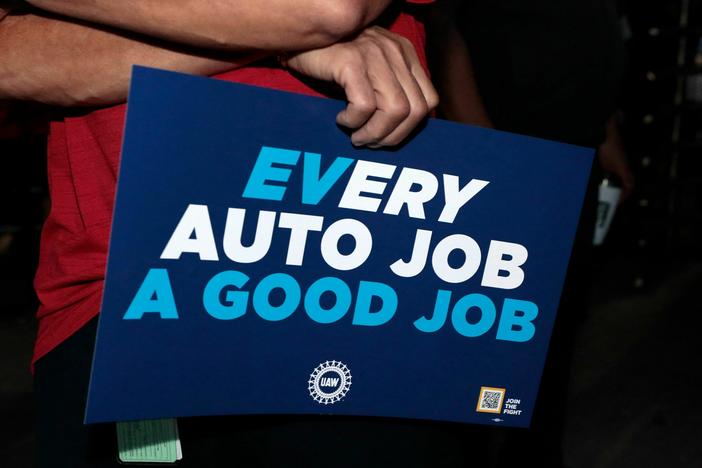 UAW supporters and members hold signs outside the Stellantis Assembly Plant in Sterling Heights, Mich., on July 12. Electric vehicles may not be at the heart of the contract talks between the UAW and the Detroit automakers, but as the sign subtly shows, they loom large in the negotiations.