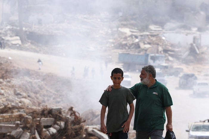 A father walks with his son in Derna, Libya, with smoke caused by a sanitation truck visible in the background. Concerns are rising about the spread of infectious diseases after fatal floods in Derna earlier this month.