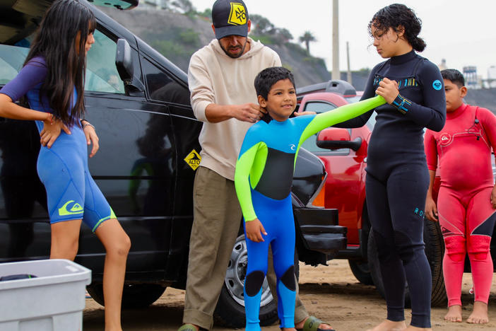 Boran Bumovich Hignio, a 7-year-old surfer, gets help with his wetsuit from Diego Villarán, who founded the local surf school, and other staffers.