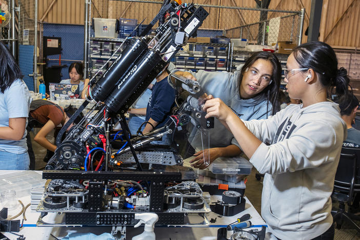 Claire Montegut (second from right), 16, and Anika Zhou (right), 17, are members of the Space Cookies, a <em>FIRST</em> Robotics Competition team composed of all Girl Scouts. Here they fix their robot's roller "claw" designed to pick up cones and cubes to score points.