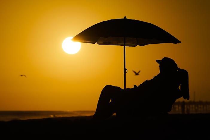 A person rests under an umbrella as the sun sets, Sept. 12, 2023, in Newport Beach, Calif. After a summer of record-smashing heat, warming somehow got even worse in September as Earth set a new mark for how far above normal temperatures were, the European climate agency reported.