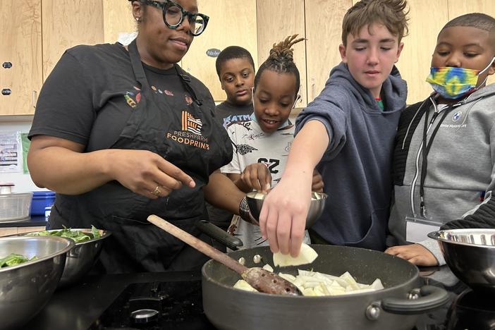 Students help instructional coach Regina Green caramelize onions for a dish featuring fresh greens from the school garden at Watkins Elementary.