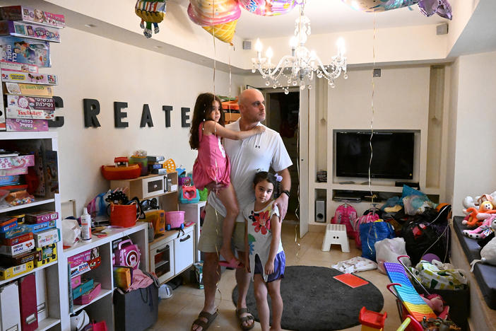 Ido Dan, an uncle to three children feared abducted by Hamas and taken to Gaza, stands for a portrait with his twin daughters. The remnants of their sixth birthday party, which took place the same day as the incursion, are still around the house.