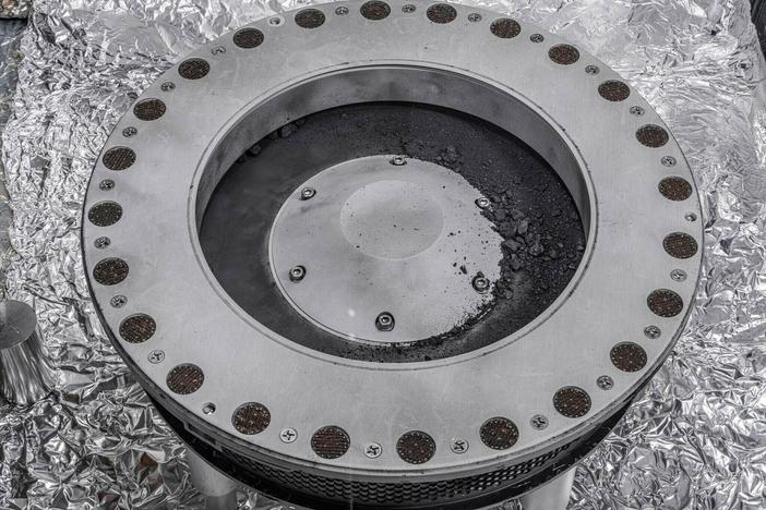 Small rocks and dust from an asteroid, outside a round sample collection device in a NASA lab.