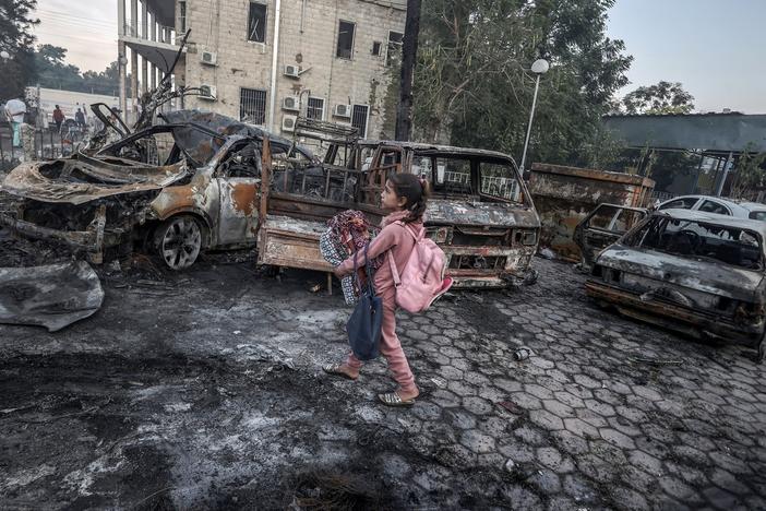 A girl tries to collect usable belongings amid the wreckage of vehicles after the explosion at Al Ahli Arab Hospital in Gaza.