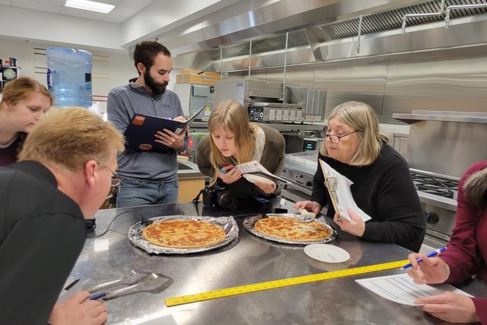 Cheese testers lean in to inspect pizzas at the University of Wisconsin's Center for Dairy Research in Madison.