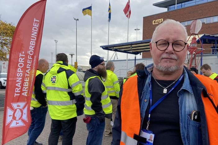 Goran Larsson, a cargo ship inspector, poses next to the Transport Workers' Union flag at the Malmo port on Nov. 7. Dockworkers are refusing to load or unload Teslas at this port and all others across the country.