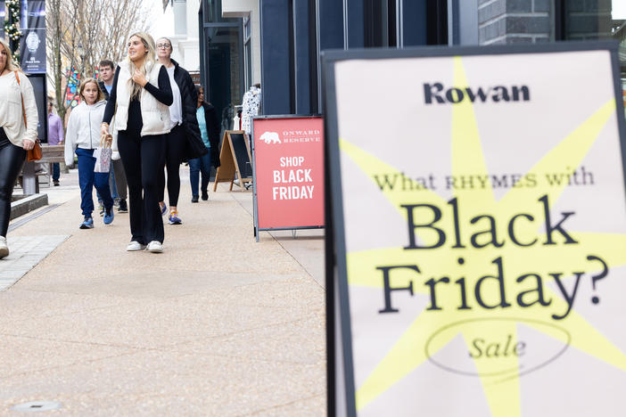 Shoppers walk past sale signs at the Avalon shopping center in Alpharetta, Ga., during Black Friday in 2022.