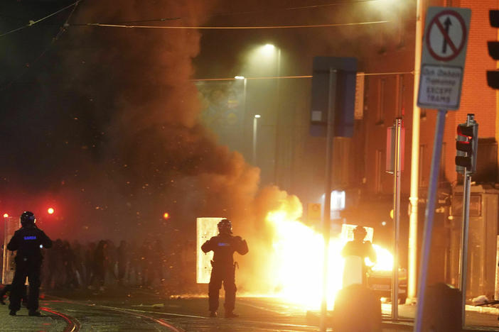 A car burns as Irish policemen stand at the scene of an attack in Dublin city centre, Thursday Nov. 23, 2023.