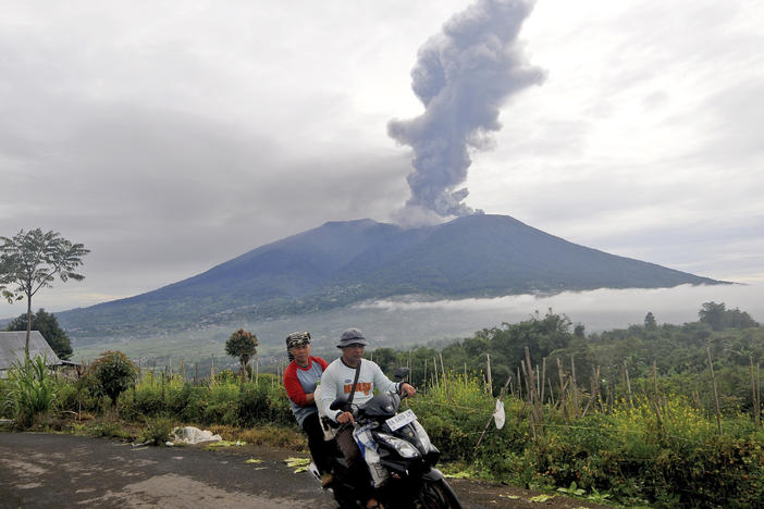 Motorists ride past by as Mount Marapi spews volcanic materials during its eruption in Agam, West Sumatra, Indonesia, Monday, Dec. 4, 2023.