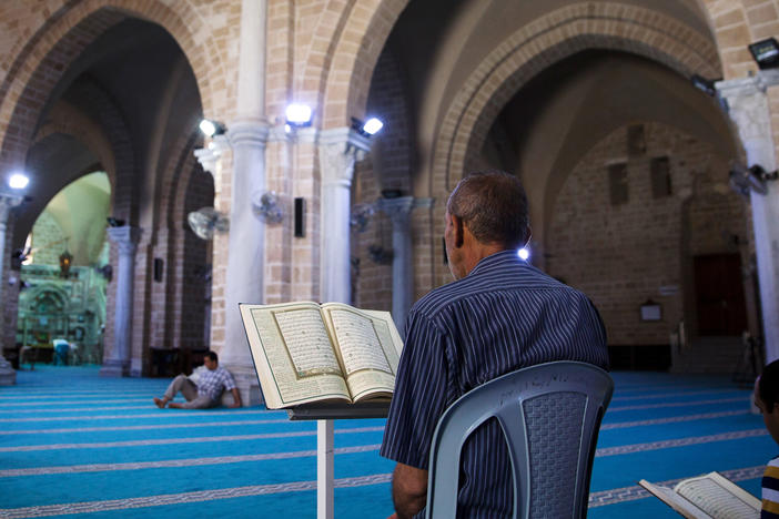 Left: A Palestinian schoolgirl in Gaza City passes by the main entrance to Pasha's Palace in 2019 as the minaret of the Omari Mosque is seen in the background. Right: Palestinians spend a Ramadan fasting day in 2019 reading the Quran inside the Omari Mosque.