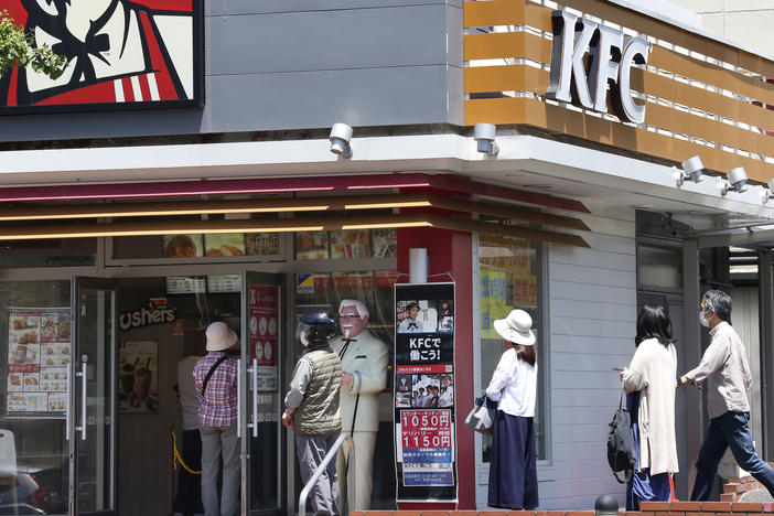 People wearing face masks to protect against the spread of the new coronavirus keep social distancing as they wait to enter a KFC restaurant in Yokohama near Tokyo on May 14, 2020.