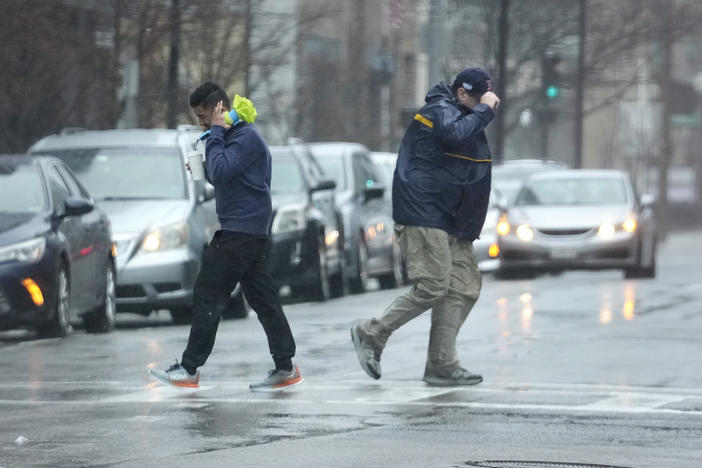 Pedestrians are buffeted by wind as they cross a street Monday in Boston.