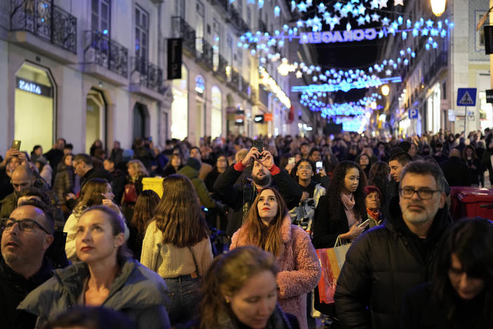 People look up at Christmas lights as crowds stroll around downtown Lisbon's Chiado neighborhood, on Saturday, Dec. 23, 2023.