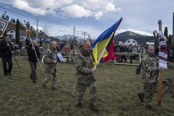 Ukrainian servicemen carry national flags and photos of their comrade Vasyl Boichuk, who was killed in Mykolayiv in March 2022, during his funeral ceremony at the cemetery in Iltsi village in Ukraine on Dec. 26, 2023.