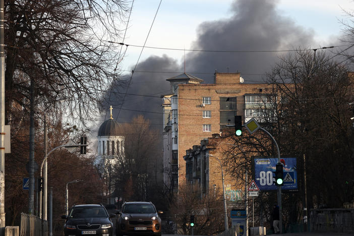 Cars drive down the street while smoke rises from a fire after a rocket attack in the centre of Kyiv on Dec. 29, 2023.