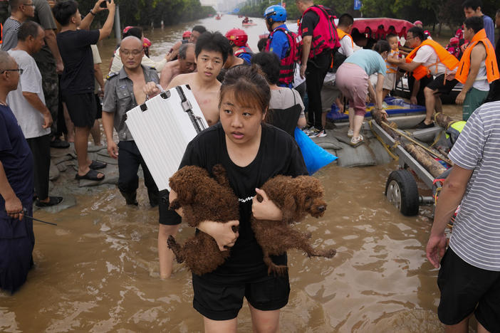 A woman carries her pet dogs as residents are evacuated on rubber boats through floodwaters in northern China's Hebei province in August 2023 amid severe flooding from Typhoon Doksuri. 2023 was the hottest year ever recorded, scientists say.