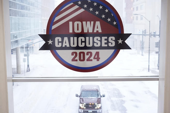 A pickup truck is driven down a snow-covered road under an Iowa caucuses sign on Friday in downtown Des Moines, Iowa.