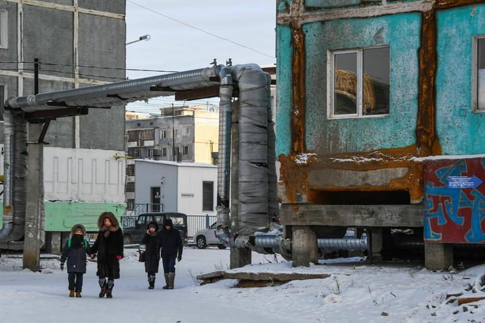 People walk next to a cracked panel apartment building in the eastern Siberian city of Yakutsk in 2018. Climate change is causing permafrost, or permanently frozen ground, to thaw across the Arctic. When the earth thaws, it can destabilize building foundations, roads, pipelines and other infrastructure.