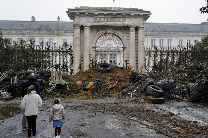 People watch slurry, manure and tyres dumped by farmers at the entrance of the local state administration building, in Agen, southwestern France, Saturday, Jan. 27, 2024. French farmers have vowed to continue protesting and are maintaining traffic barricades on some of the country's major roads.