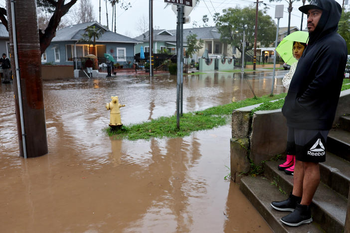 Residents stand along a flooded street in Santa Barbara, California, as a powerful atmospheric river pummels the region. The storm has caused landslides, power outages, and road and airport closures across Southern California.