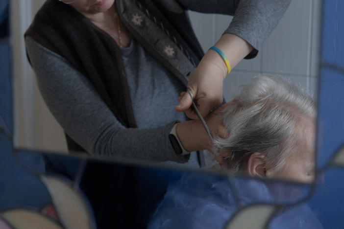 Caregiver Liliya Khodunay cuts Anna's hair in Anna's home in Milan, Italy, in February 2023.