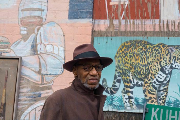 Muralist William Rankins Jr. stands in front of some of his murals in the Ollie's Trolley courtyard in Cincinnati. Ollie's is a restaurant.