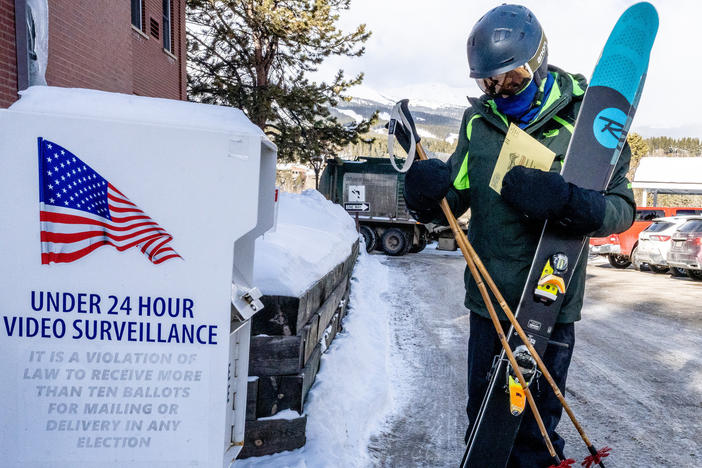 Bob Christie carrying his skis on the way to the slopes in Breckenridge, Colo., drops off his ballot on March 5, 2024.
