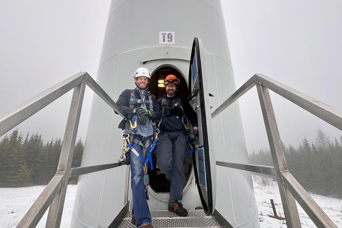 Reporter Darian Woods and wind turbine technician Konnor Therriault at the base of a Vestas wind turbine in Bingham, Maine. (Photo by Matthew Copeman)