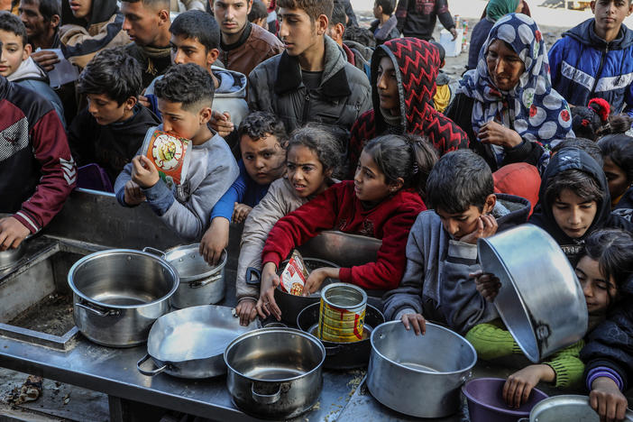 Palestinian people with empty bowls wait for food at a donation point in Rafah. A report out this week shows widespread hunger and malnutrition in Gaza but stopped short of declaring it a "famine."