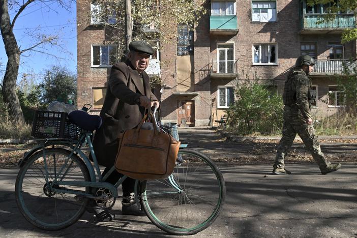 A Ukrainian policeman (R) walks next to 84-year-old resident Mykola (L) pushing his bicycle on a street in the frontline town of Chasiv Yar, in the Donetsk region on October 11, 2023, amid the Russian invasion of Ukraine. Explosions are near-constant in the small town, whose buildings are scored with holes from shelling.