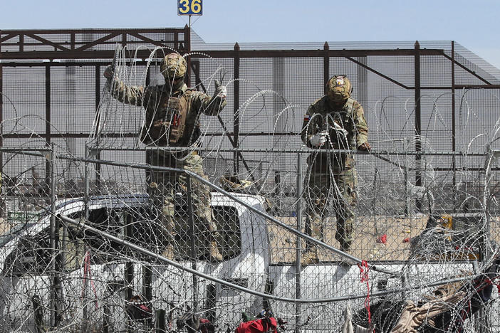 Members of the Texas National Guard placing barber wire on a fence at the border between Mexico and the US.