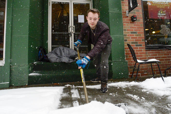 Mikey Reynolds, an employee at The Works on Main Street in Brattleboro, Vt., shovels the sidewalk in front of the restaurant as a person who is facing homelessness sleeps in a door entryway while seeking refuge from the snow storm on Saturday, March 23, 2024.
