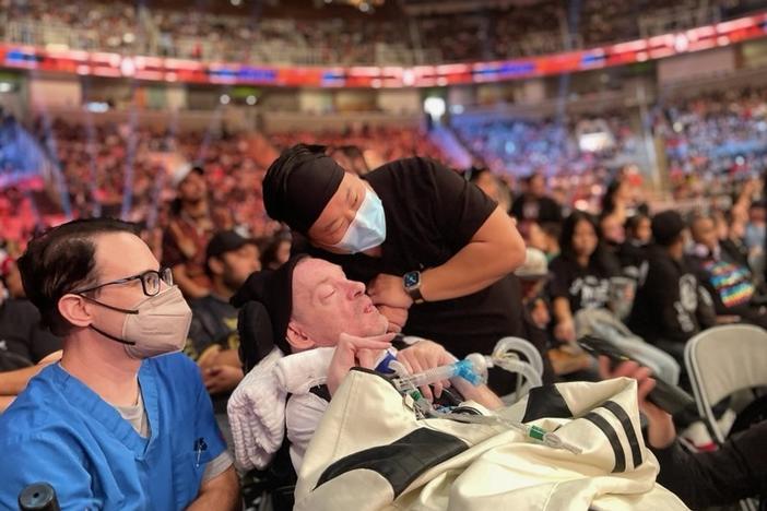 Kevin Carlson, with nurse Joshua Lee (right) and respiratory therapist Eric Mathewson (left), watches a WWE match on October 2, 2023 in San Jose, Calif.